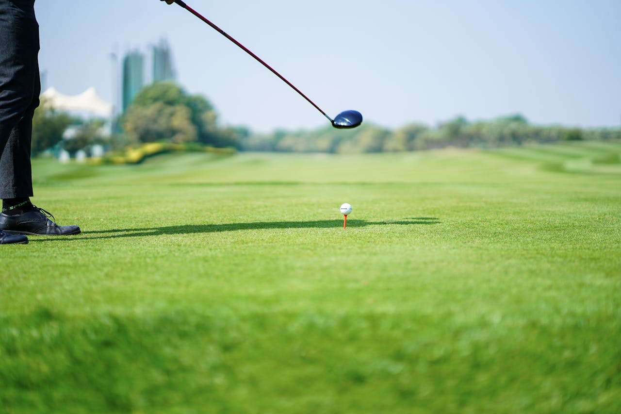 A golfer in action preparing for a tee shot on a lush green golf course under clear skies.